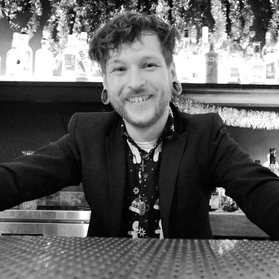 Alex, smiling behind a backlit bar